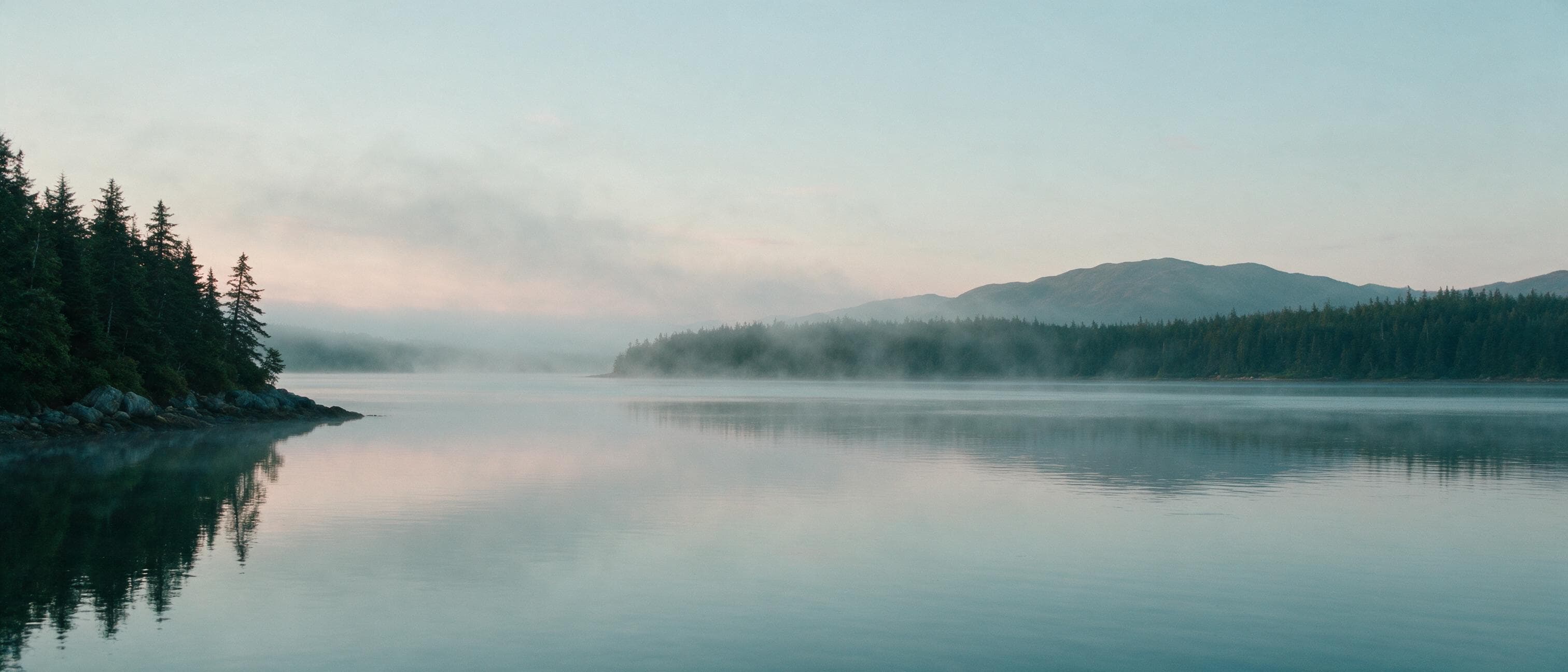 Still Alaska water at dawn, mist drifting over the surface